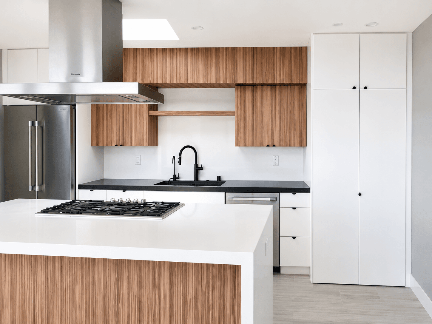 Modern kitchen with vertical wood cabinets, white island, black countertops, and stainless steel appliances.