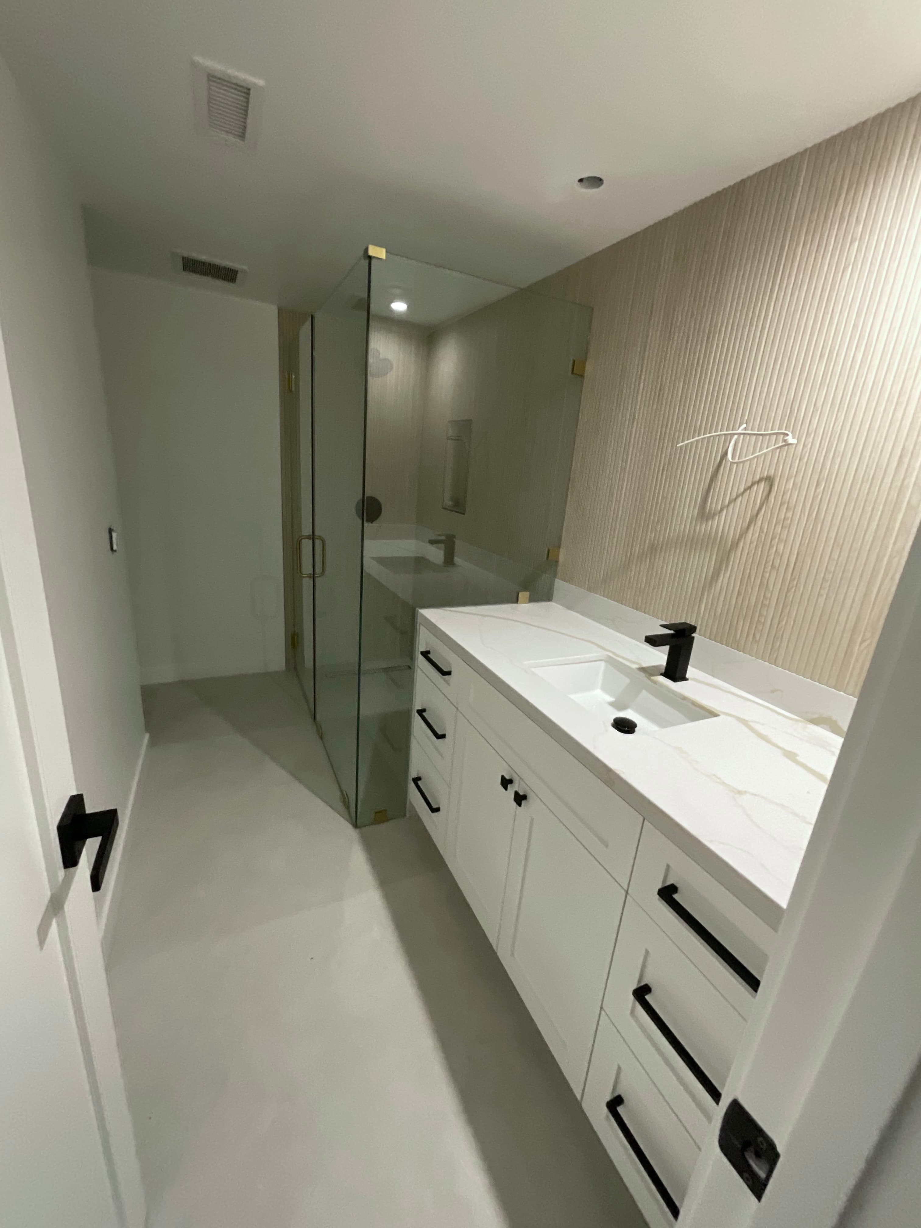 Modern bathroom featuring a white marble vanity with black hardware and a glass-enclosed shower.