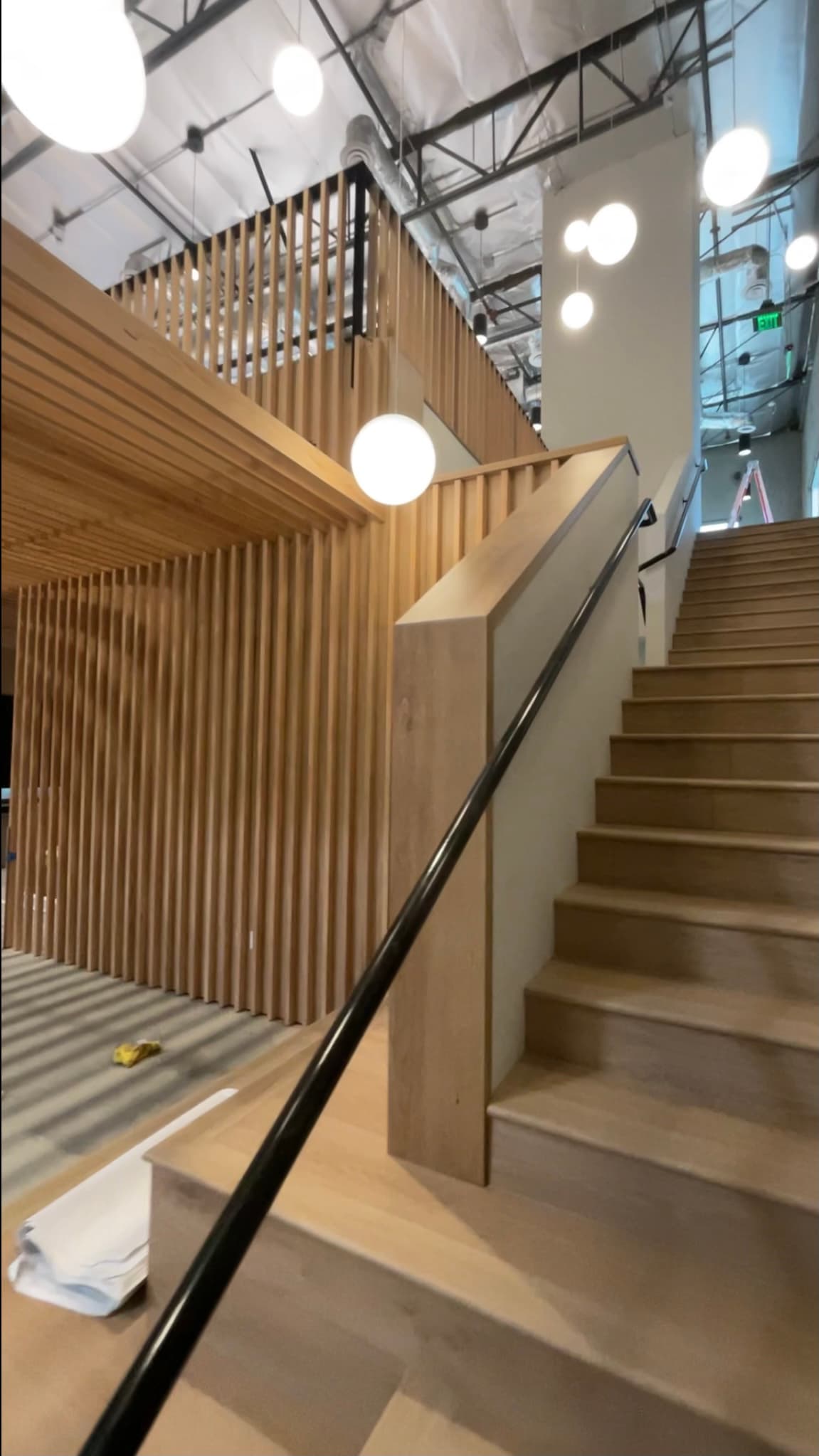 Modern wooden staircase with black railing, vertical slat wall, and hanging white globe pendant lights.