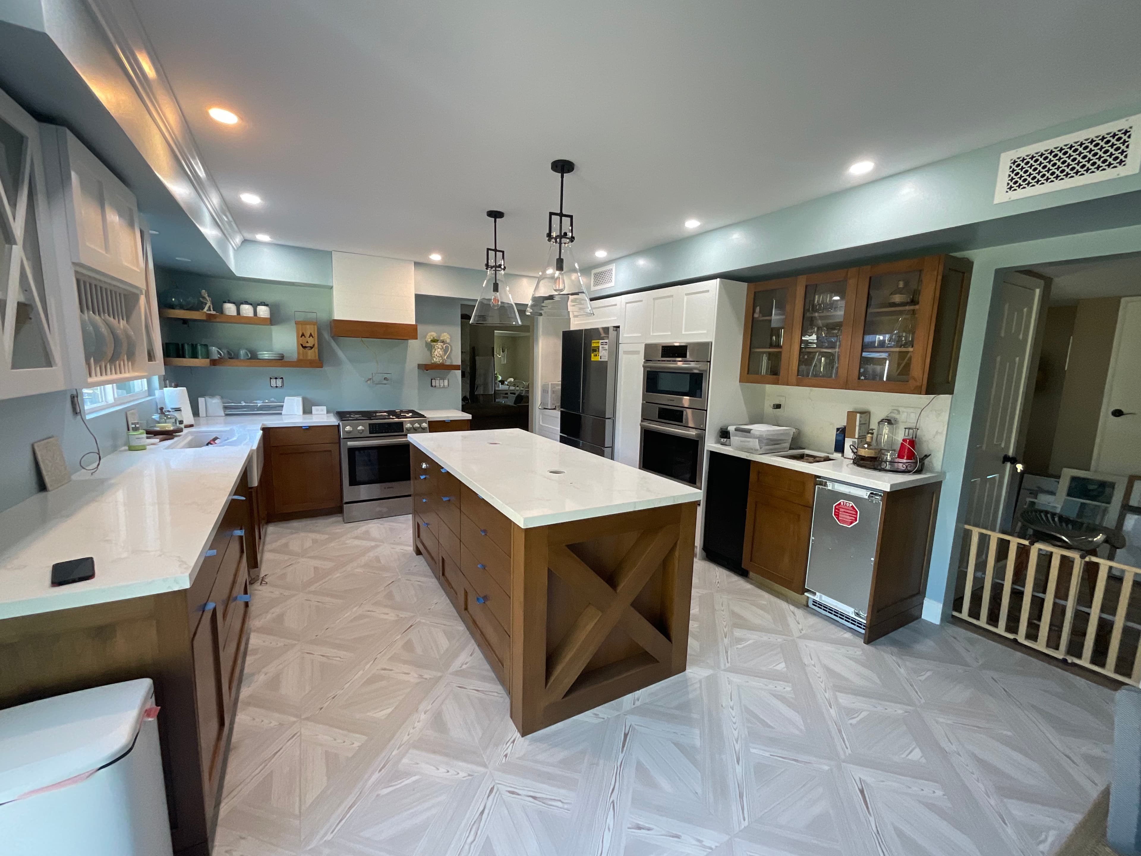 Modern kitchen featuring a wooden island, white countertops, stainless steel appliances, and light blue walls.
