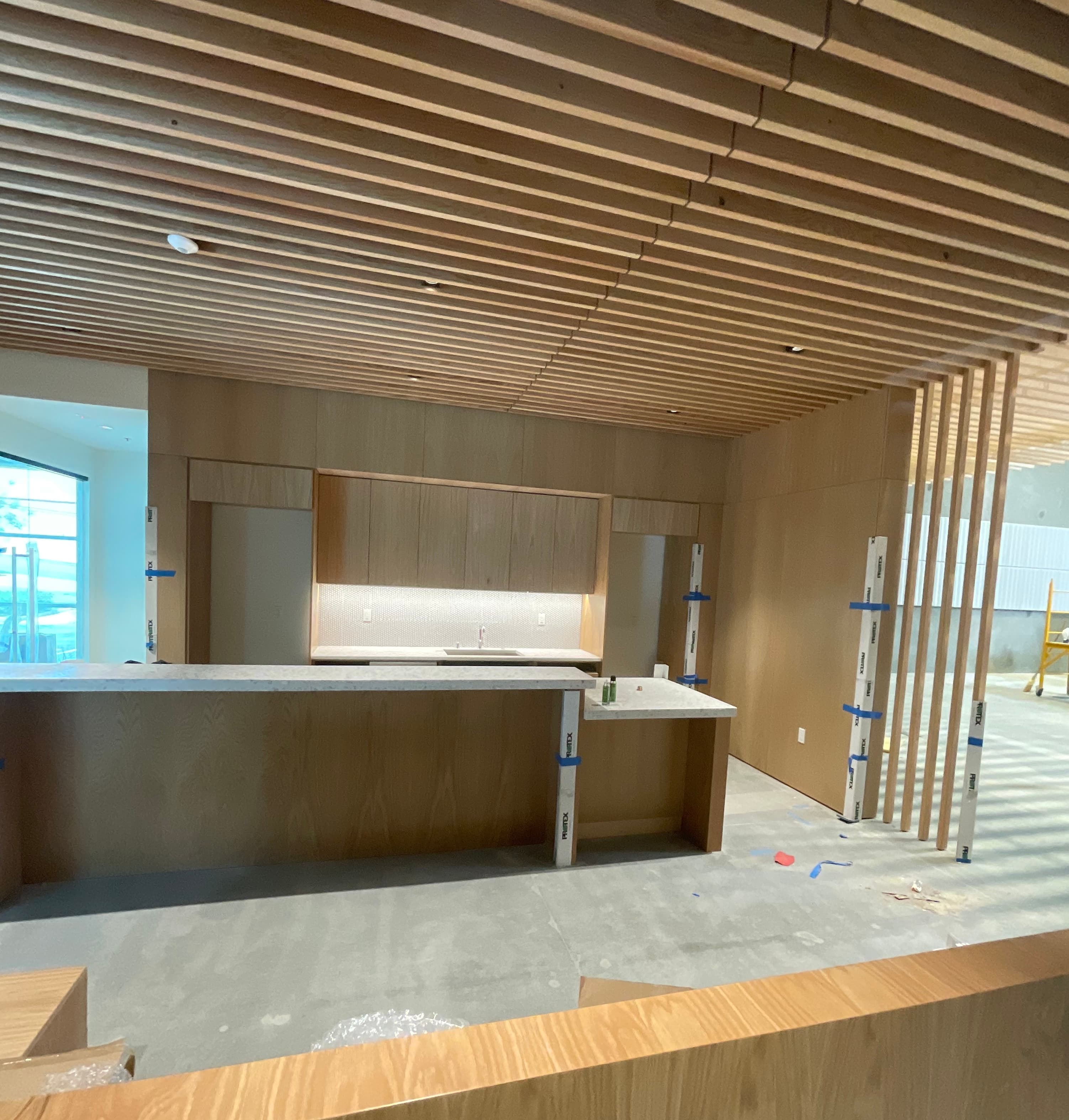 Modern wooden kitchen area under construction with slatted ceiling, wood paneling, and marble countertops.