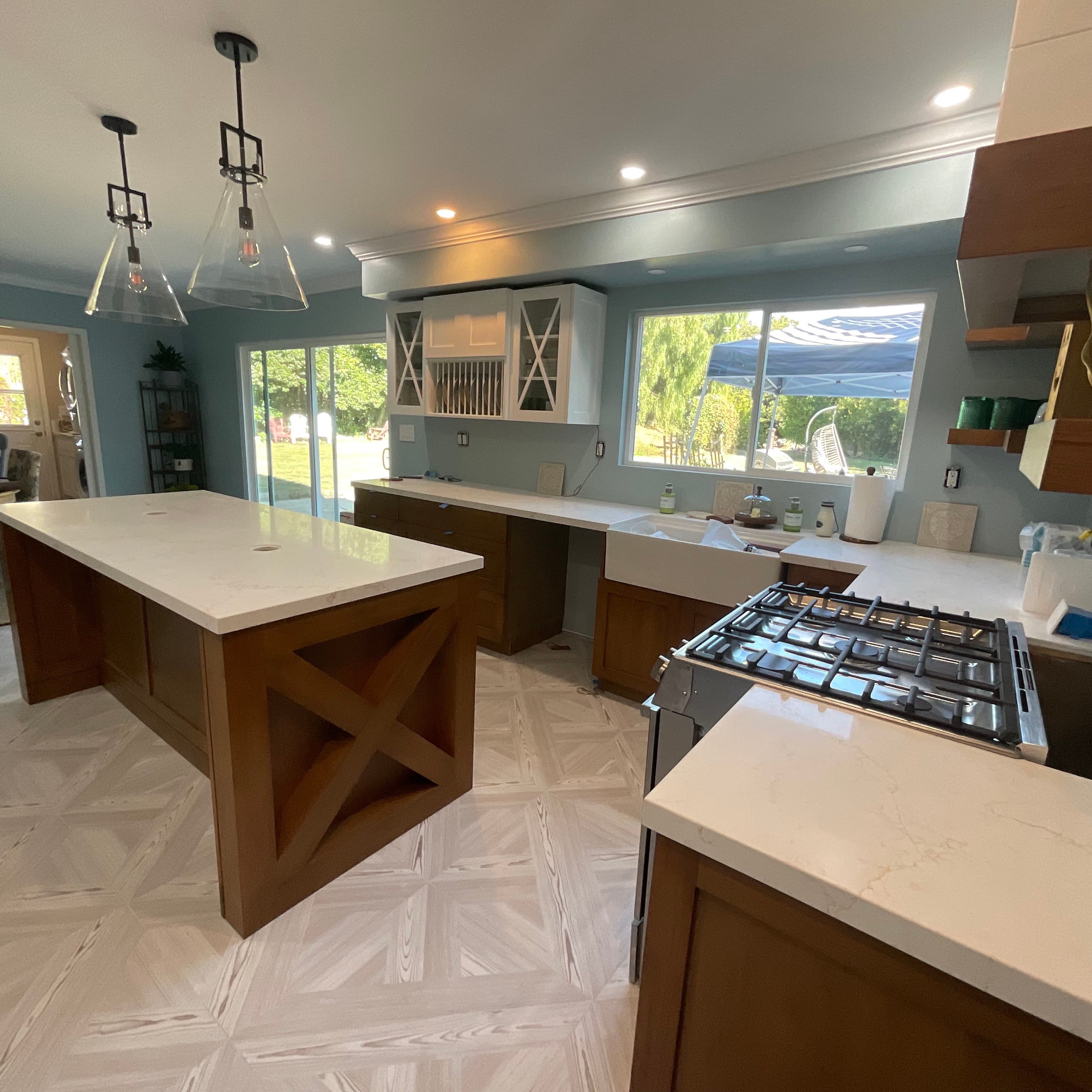 Modern kitchen with a large wood island, light blue walls, and light geometric parquet floors.